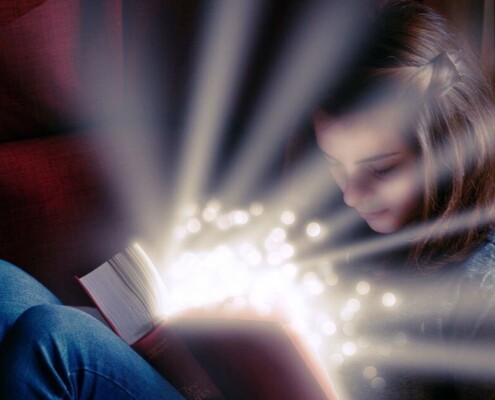 Small child reading a book with sparking light emanating from pages