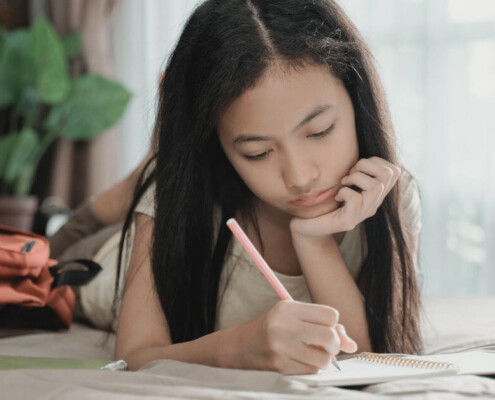 Young teen girl on bed doing homework