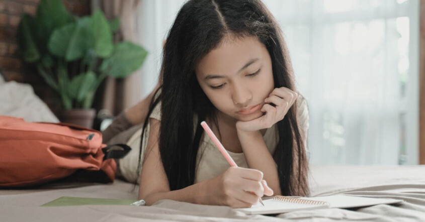 Young teen girl on bed doing homework