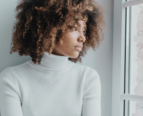 A thoughtful young Black woman looking out the window. If you're struggling with anxiety, life changes, your identity, reach out to us today. We offer compassionate young adult therapy in Medford, NJ.