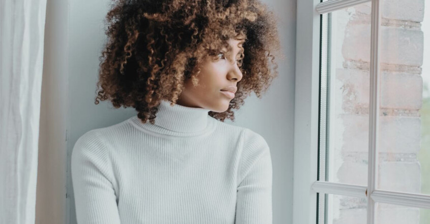 A thoughtful young Black woman looking out the window. If you're struggling with anxiety, life changes, your identity, reach out to us today. We offer compassionate young adult therapy in Medford, NJ.