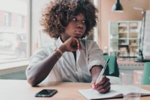 A young Black woman studying & writing down notes. Young adult therapy in Medford, NJ can help with job changes, life transitions & more. Reach out today to getpaired with a therapist. 