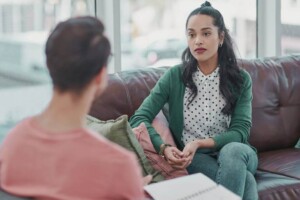 A professional woman sitting on a couch talking to another individual. Young adult therapy in Medford, NJ can help you work through stress, anxiety & burnout. Discover more here!