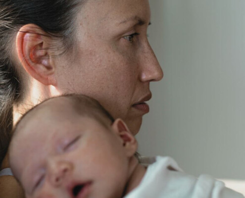 An exhausted-looking new mom holds a sleeping baby on her chest. Motherhood doesn't have to strip you from your identity. Discover how postpartum depression therapy in Haddonfield, NJ can help you find yourself.