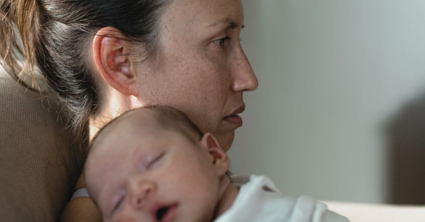 An exhausted-looking new mom holds a sleeping baby on her chest. Motherhood doesn't have to strip you from your identity. Discover how postpartum depression therapy in Haddonfield, NJ can help you find yourself.