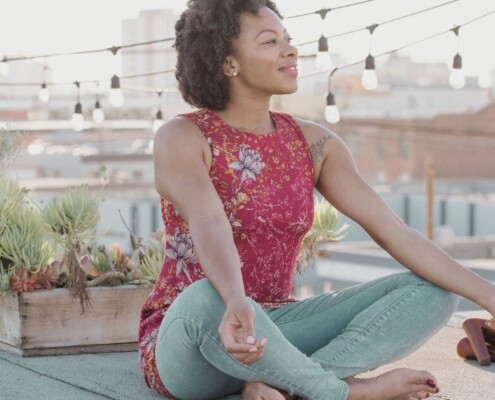 A young adult woman meditates peacefully on a rooftop at sunset.