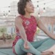 A young adult woman meditates peacefully on a rooftop at sunset.