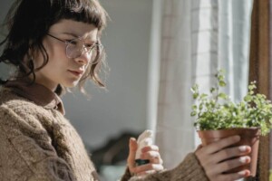 A teenager sprays water on a potted plant near a window.