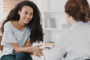 A smiling young woman talks with a therapist in a well lit room.