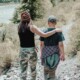 Mom and teen walk side by side on a forest trail, one with an arm around the other.