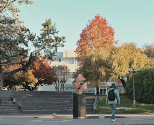 Students walk through a tree-lined campus with fall foliage.