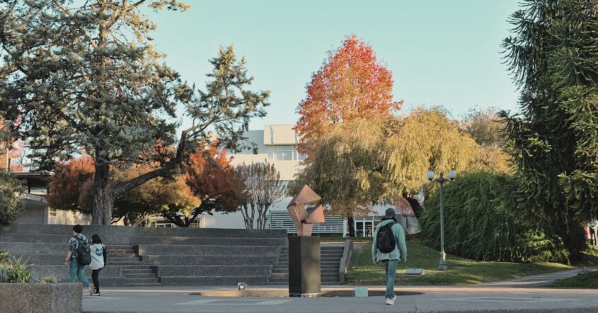 Students walk through a tree-lined campus with fall foliage.