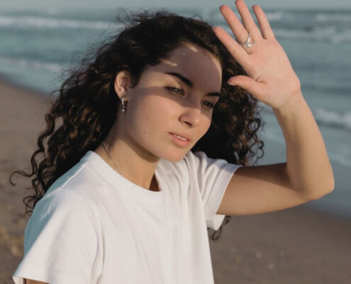 A young adult standing at the edge of a calm shoreline, looking toward the horizon.