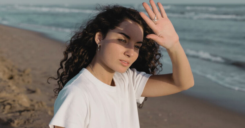 A young adult standing at the edge of a calm shoreline, looking toward the horizon.