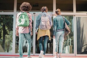 Three students with backpacks walk toward the entrance of a school.