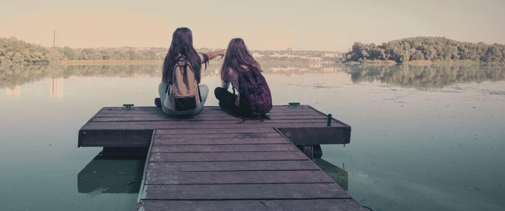 Two teen girls sitting on a dock pointing to the water while wearing backpacks. If your child is struggling with back to school anxiety, our teen therapists in Medford, NJ can help. Reach out today to start the therapy journey.