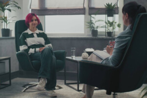 A teen with pink hair sits in a therapy session, facing a therapist with a notebook. Teen therapy in Medford, NJ can help your teen with back to school anxiety. Learn how our therapists can support you today!