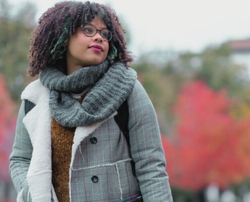 A student walks through a tree-lined campus with fall foliage.