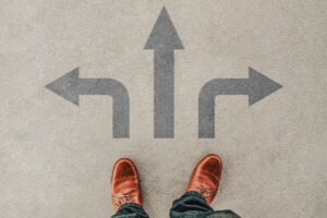 Feet standing in front of arrows pointing left, straight, and right on pavement.