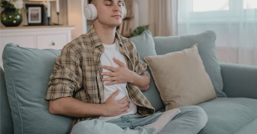 A young adult meditating with headphones on a couch.