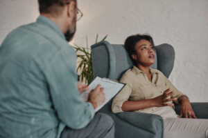 A college age woman talking to a therapist with a clipboard.