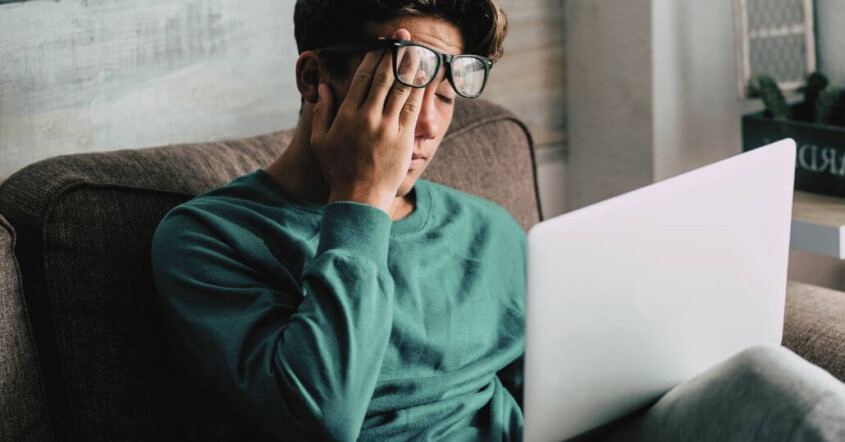 A college student sits on a laptop looking overwhelmed.