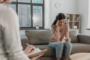 An upset young woman holding a glass of water during a therapy session.