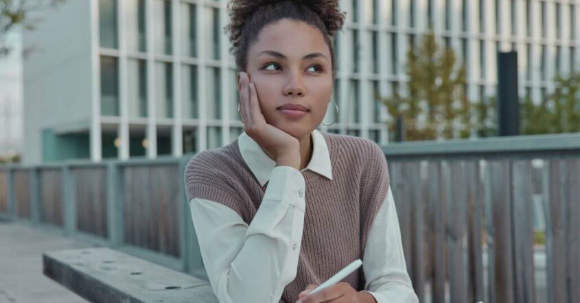 Young college student sitting outdoors, thoughtfully journaling.