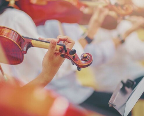 Close-up of musicians playing violins in an orchestra, with hands on the strings and bows moving in unison.