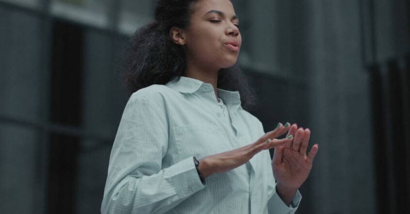 A woman stands outdoors with her eyes closed, taking a deep breath while holding her hands in a relaxed, grounding position. Representing how ADHD therapy in Medford, NJ can help you feel more grounded with executive functioning skills. Learn more here.