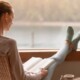 Woman reading a book while resting her feet on a windowsill. Representing how beginning therapy in January can help you reach your goals in a supportive way. Contact us today to start healing.