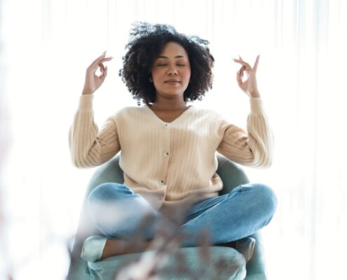 Woman sitting cross-legged in a chair with eyes closed, practicing mindfulness at home