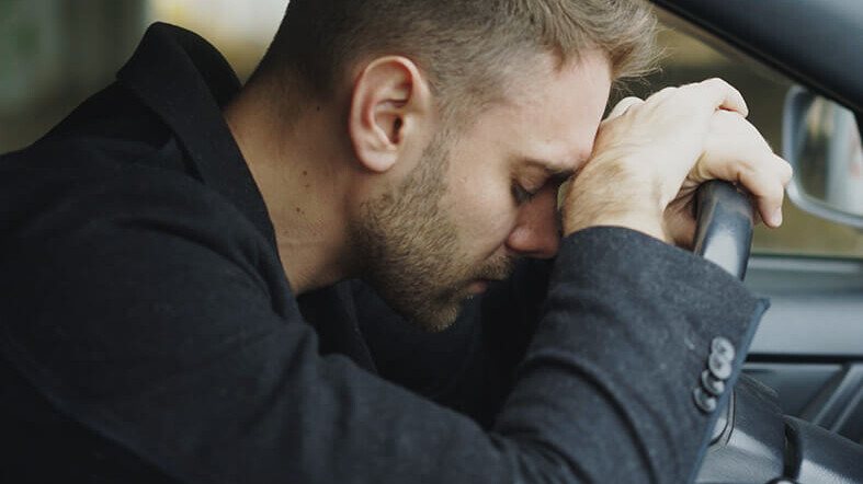 Stressed man resting his head against a steering wheel in car. This represents how stress & anxiety can affect men differently. Learn how men's counseling in Medford, NJ can help you.