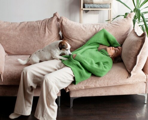 Exhausted woman lying on couch with dog showing emotional fatigue and mental load burnout at home