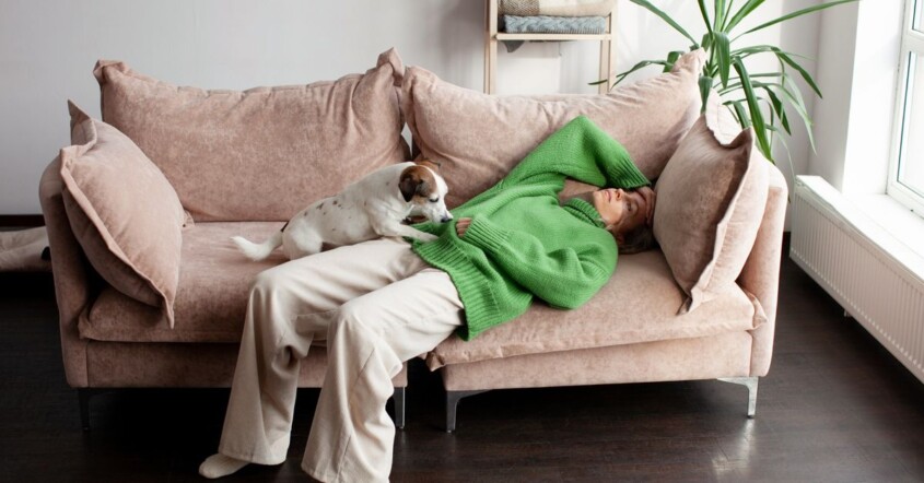 Exhausted woman lying on couch with dog showing emotional fatigue and mental load burnout at home